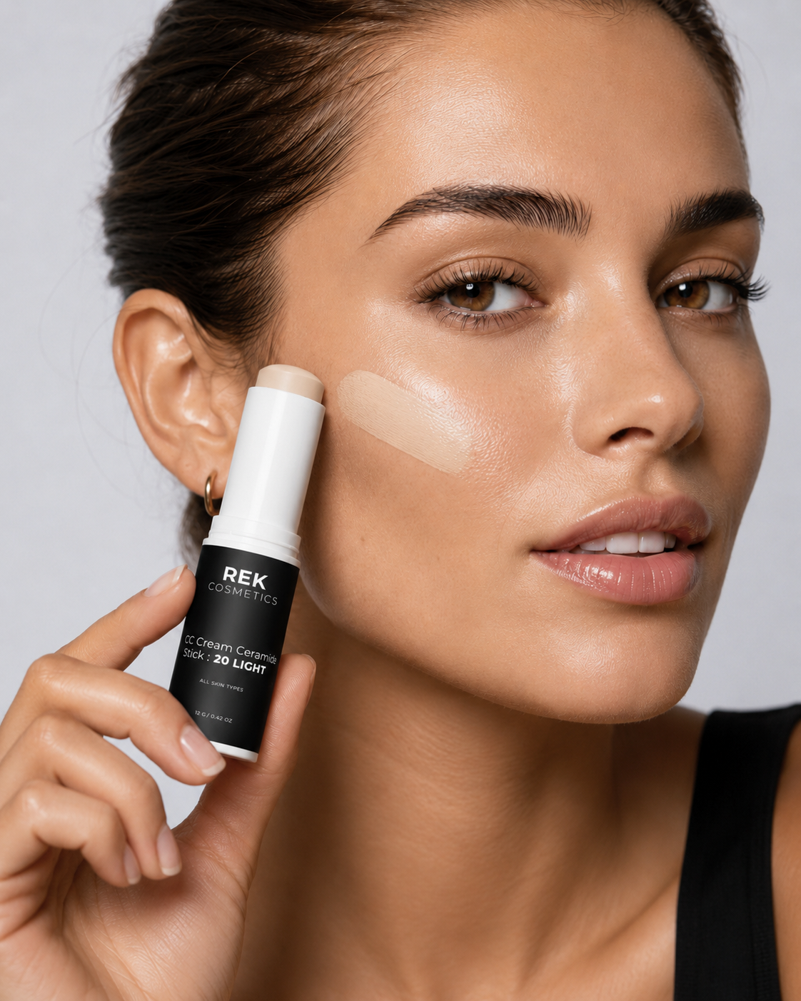Woman applying REK Cosmetics concealer to her face against a neutral background