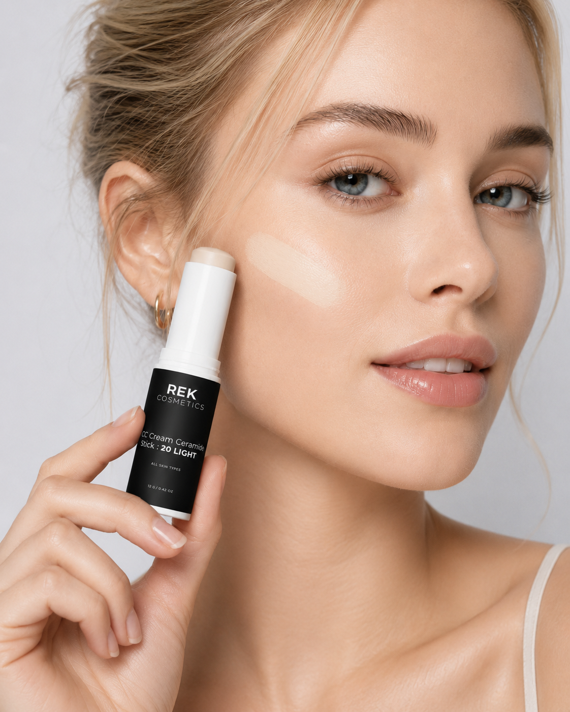 Woman holding a REK Cosmetics concealer bottle against a neutral background