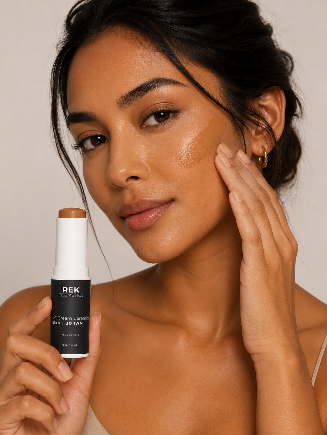 Woman applying makeup with a REK product on a neutral background